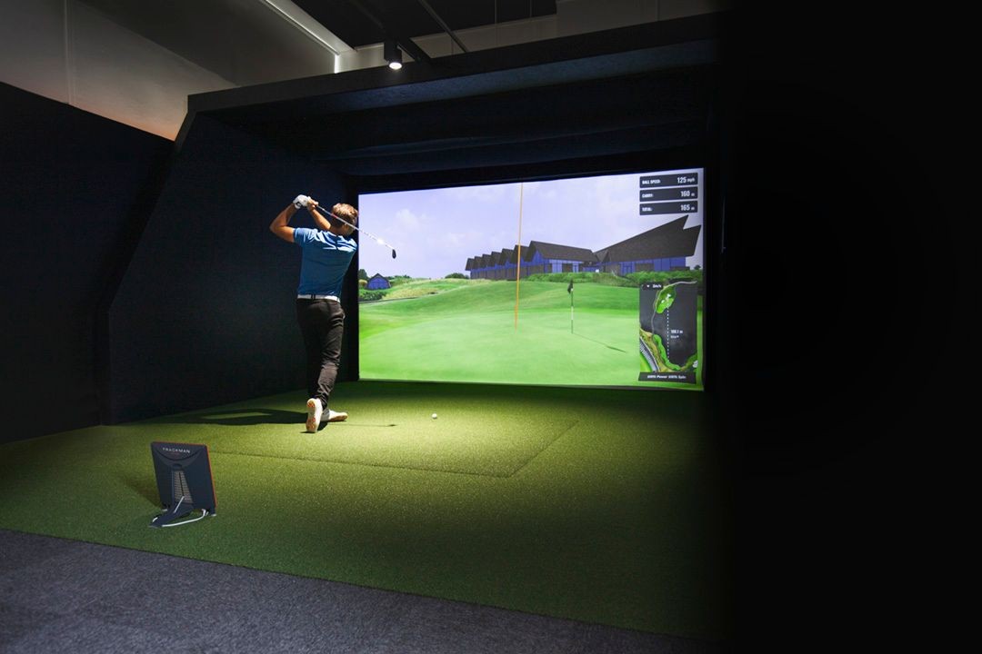 Person playing golf in an indoor simulator with a virtual green on the screen.